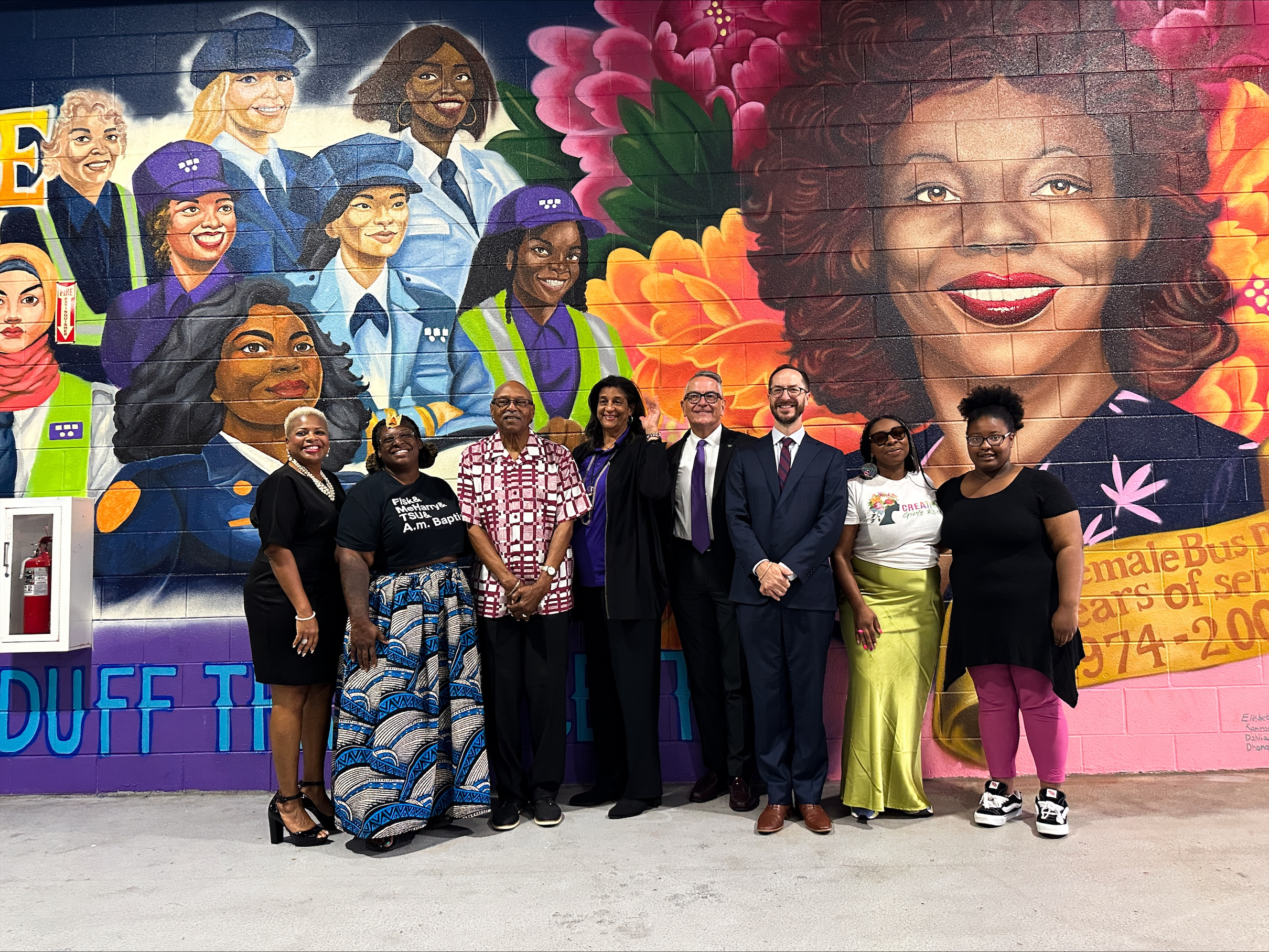 A group of people pose in front of a mural at the Elizabeth Duff Transit Center at WeGo Central