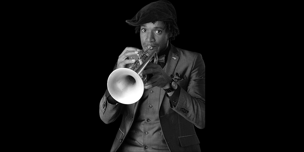 Black and white image of a trumpet player wearing a suit and hat, focused intently on playing