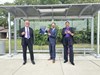 Three people stand smiling at a bus stop ribbon-cutting ceremony