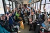 A group of people sit in a bus, smiling and raising their hands in a cheerful, celebratory manner